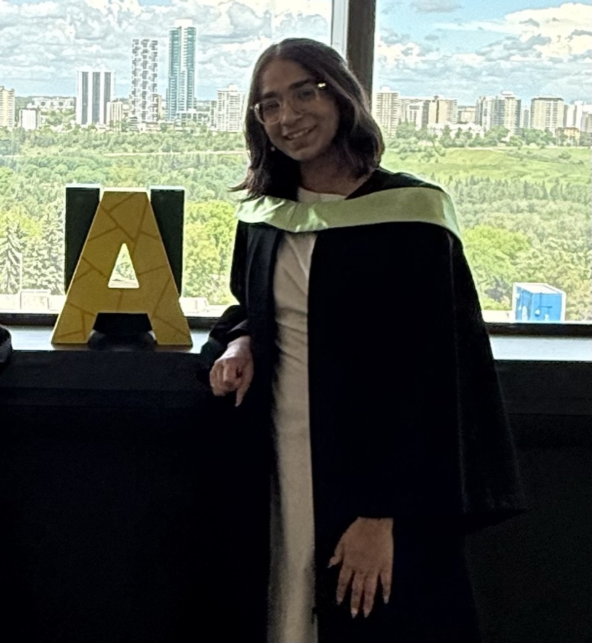 Diyaa in convocation robes beside the University of Alberta letter sculpture